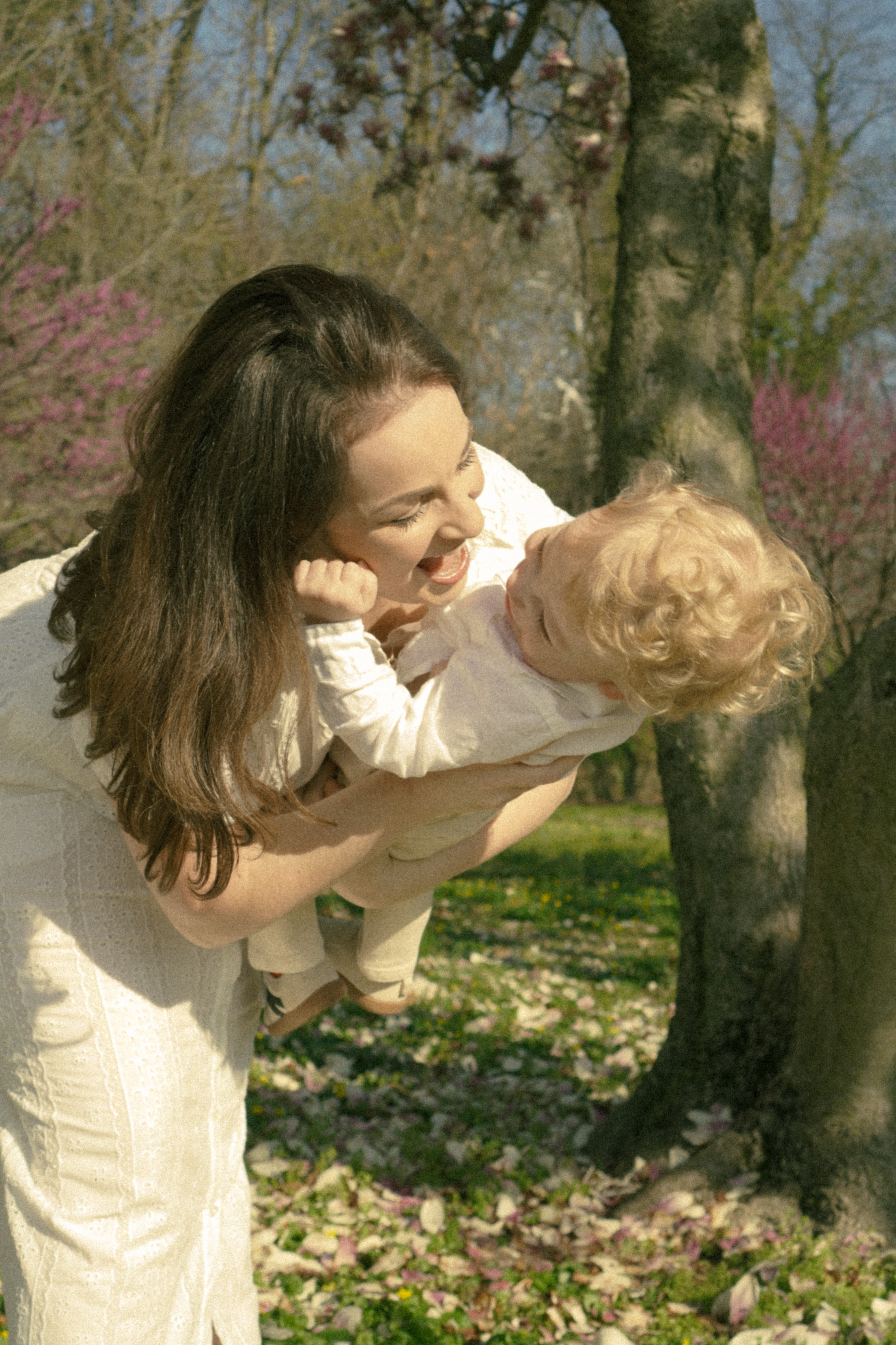 Mom lifting her curly-haired son among magnolia trees