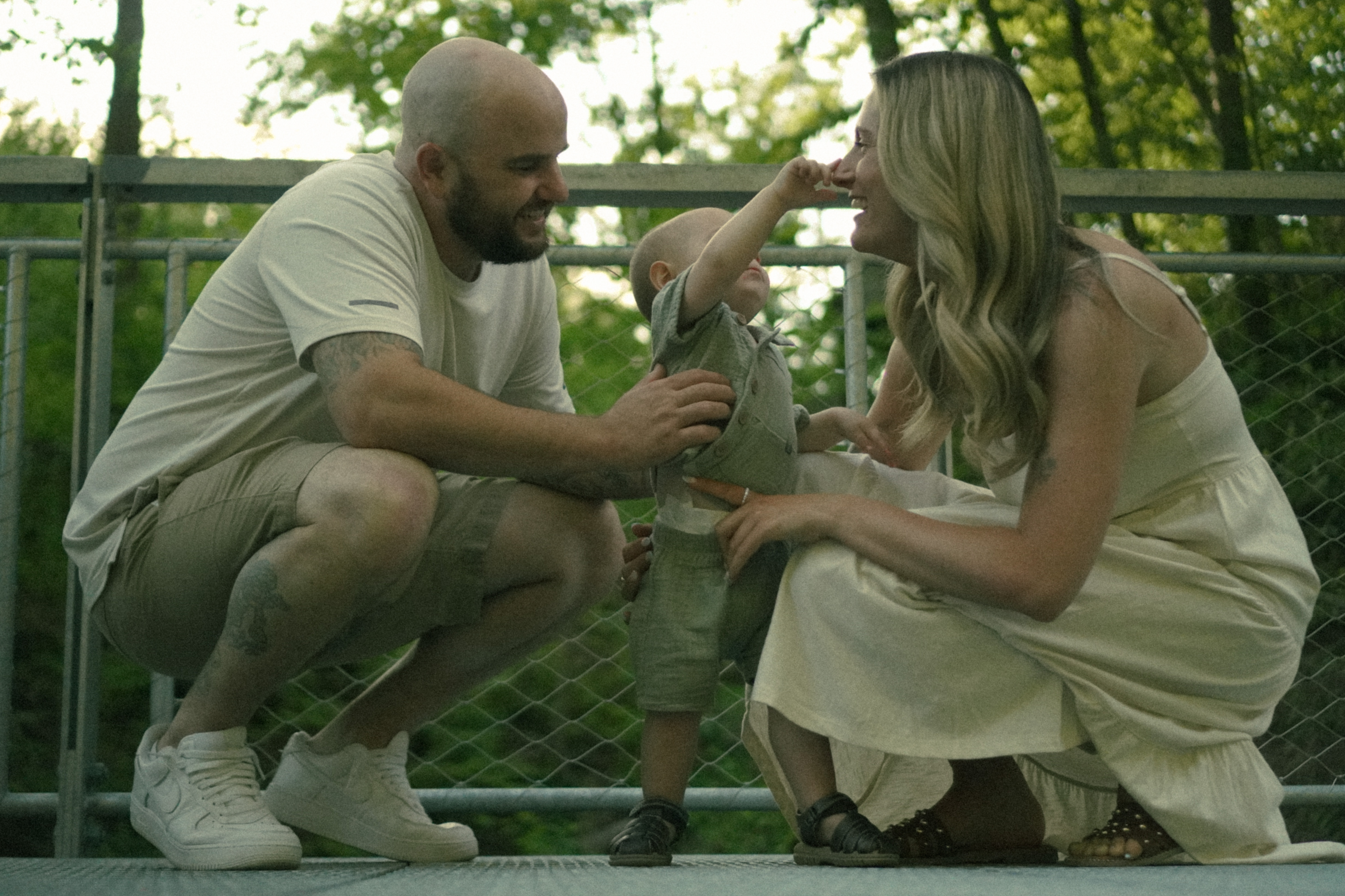 Parents kneeling with their toddler on a bridge surrounded by green